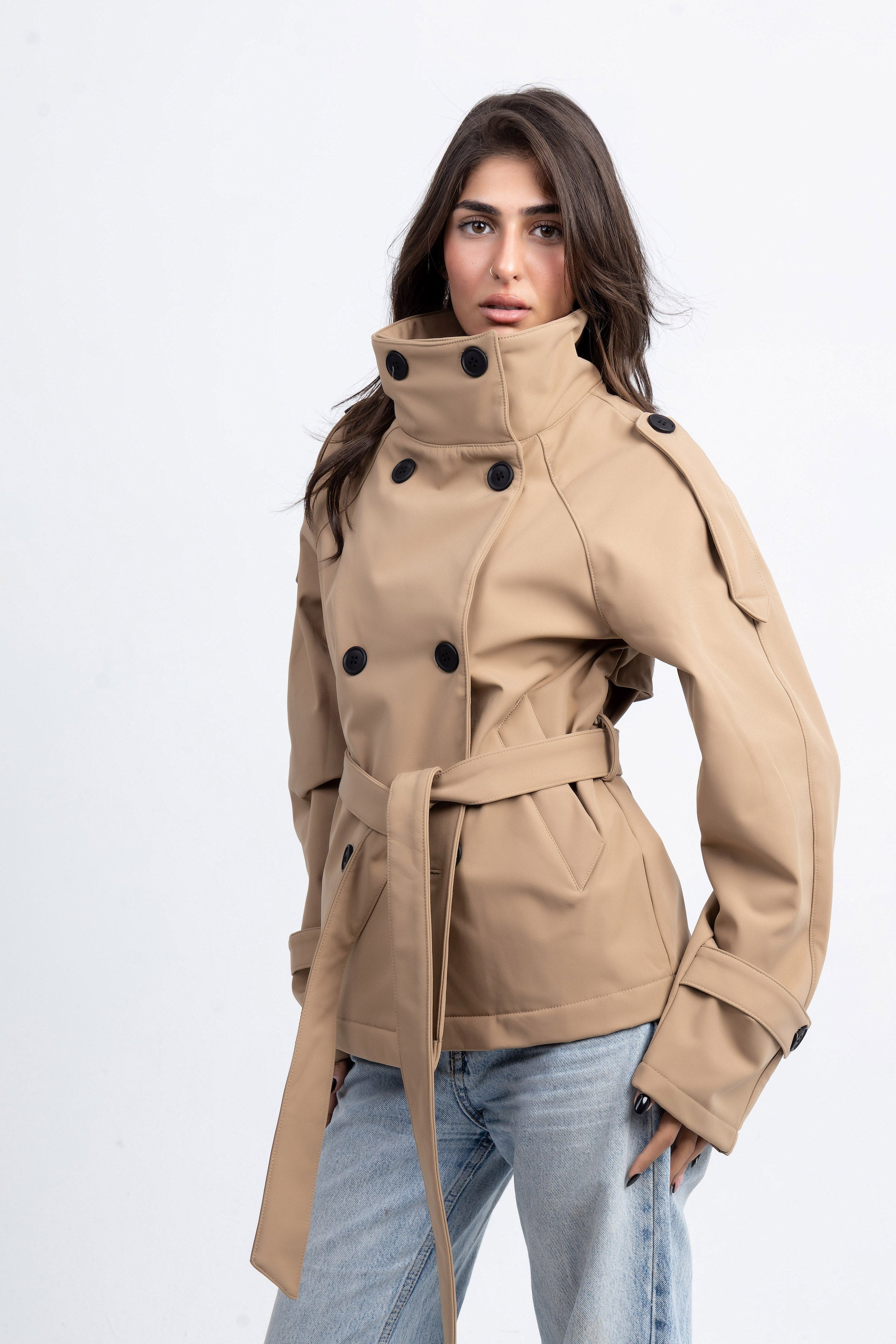 Woman wearing a beige trench coat with black buttons on a white background
