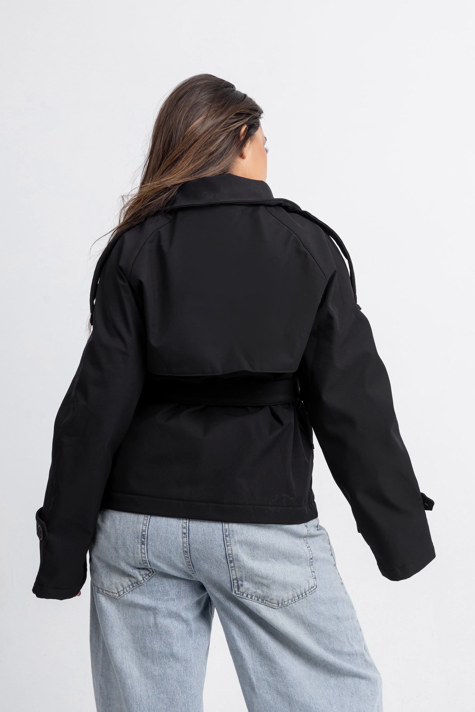 Person wearing a black jacket and light blue jeans on a white background