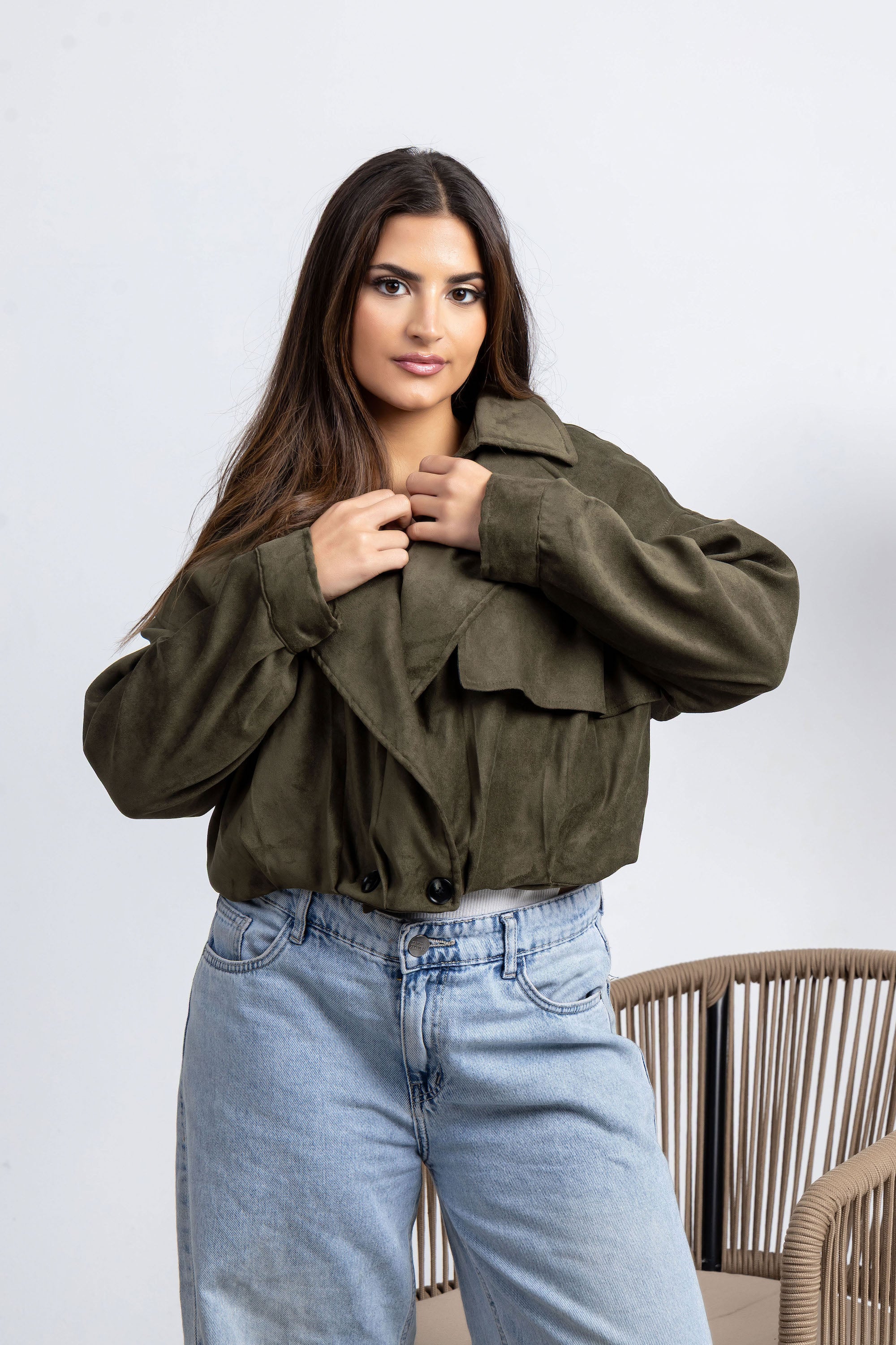 Woman wearing an olive green jacket and light blue jeans against a white background