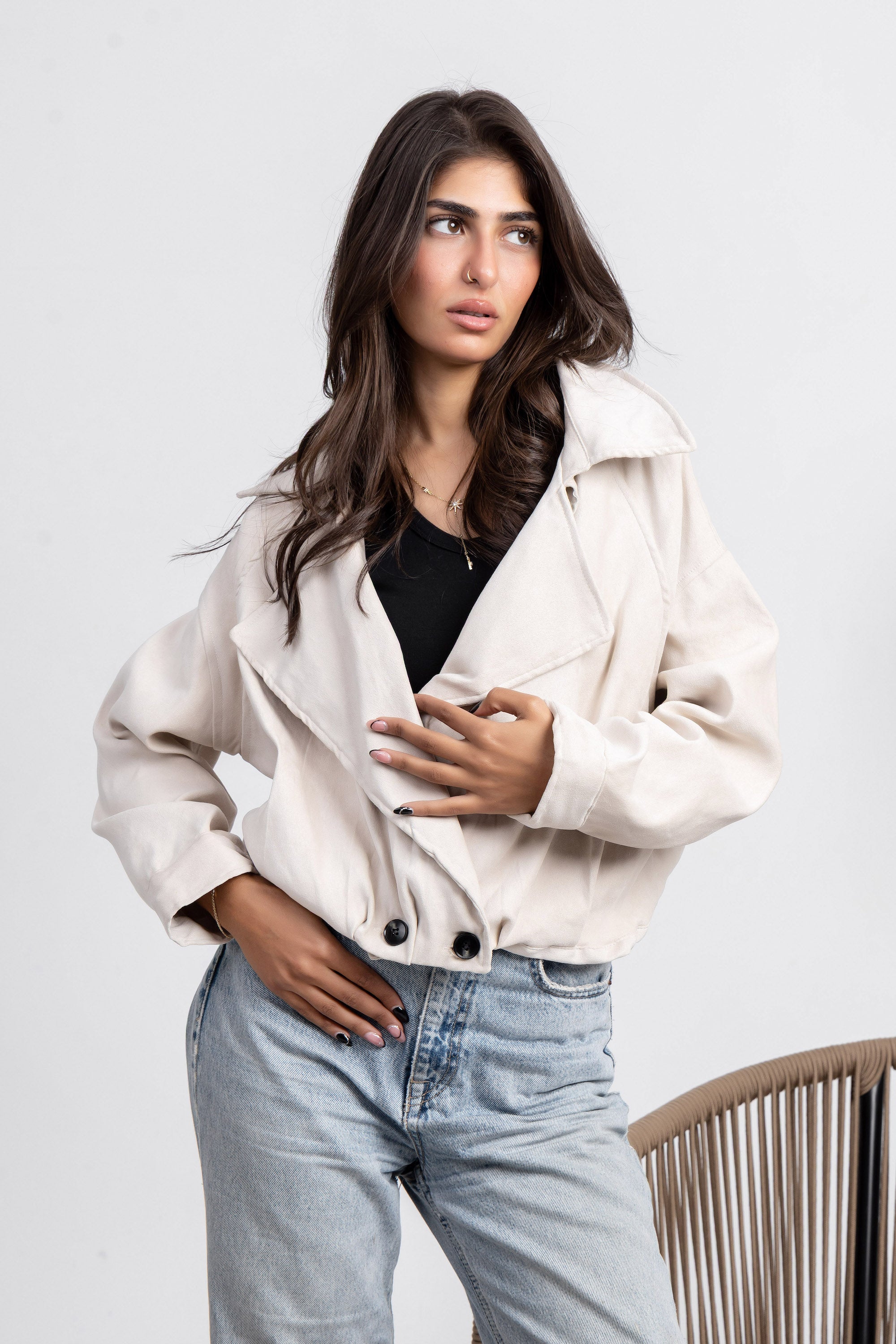 Woman wearing a beige jacket and light blue jeans on a white background