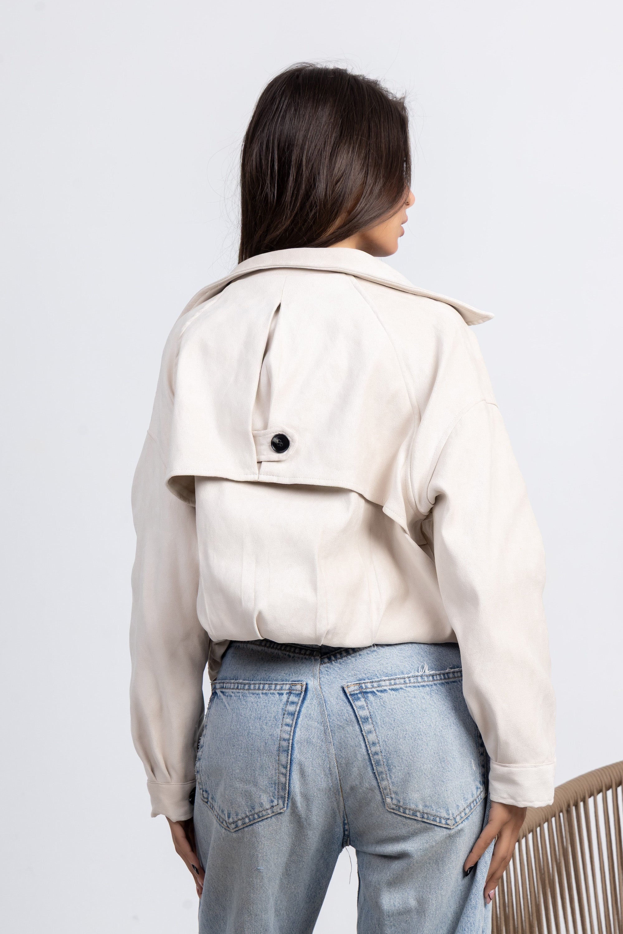 Person wearing a beige jacket and light blue jeans on a white background